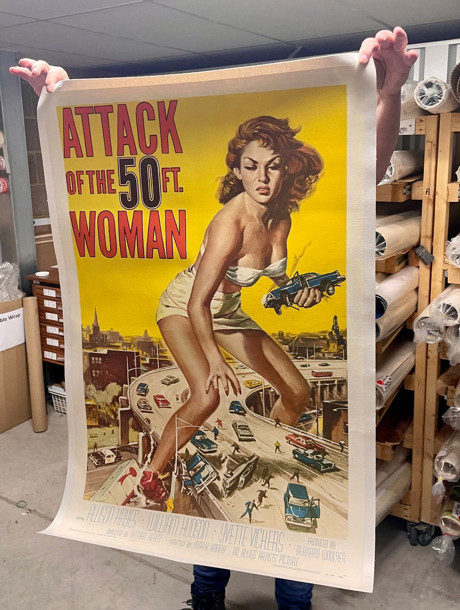 An unframed original Attack of the 50 Ft. Woman poster held open by hand and looked over
